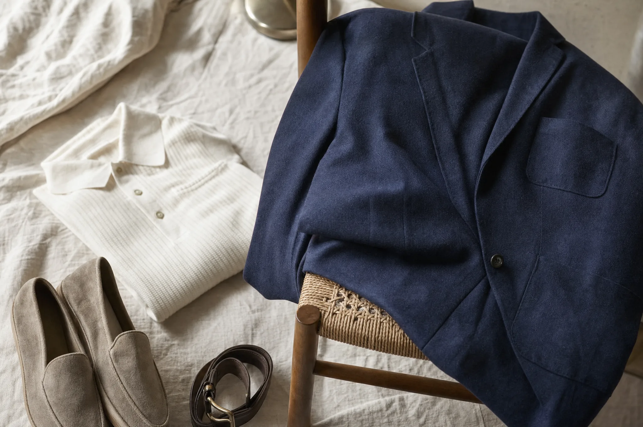 Keten yüzey üzerinde lacivert yapısız ceket, krem triko, süet loafer ve deri kemerden oluşan smart casual kombin